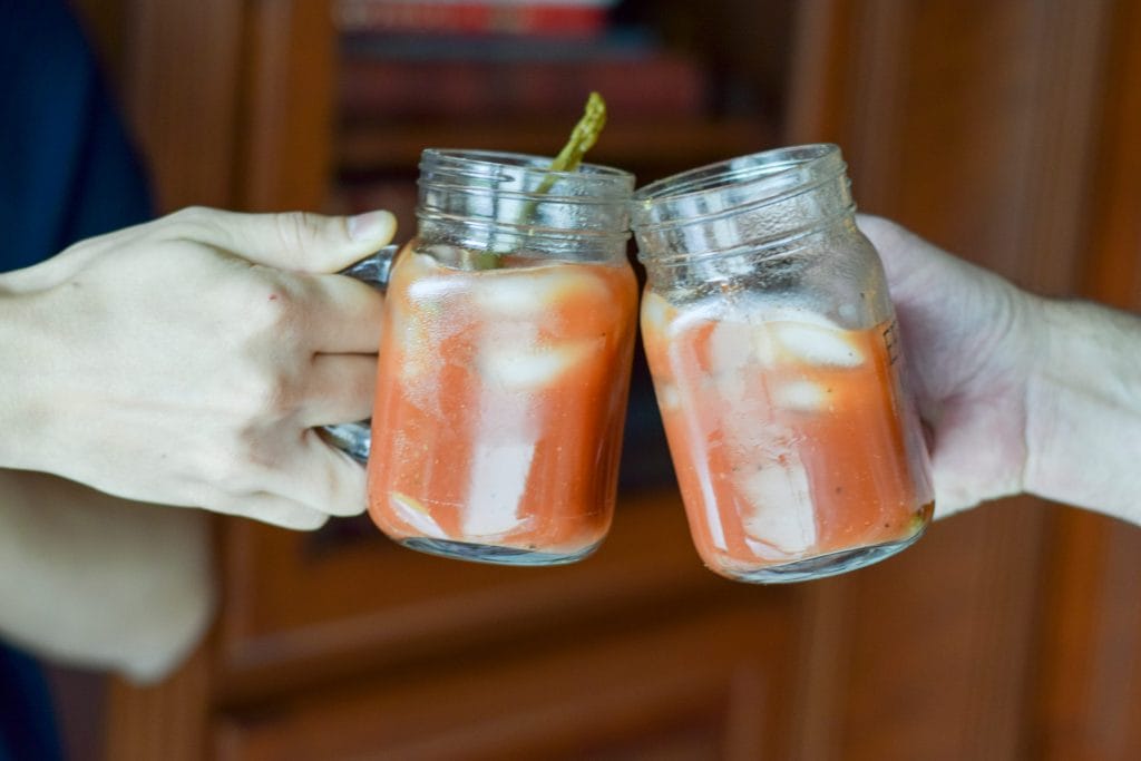 Two People Holding Mugs Full Of Bella Sun Luci Bloody Marys, Toastin The Indy 500. Winning Cocktails Enhance Exciting Events.